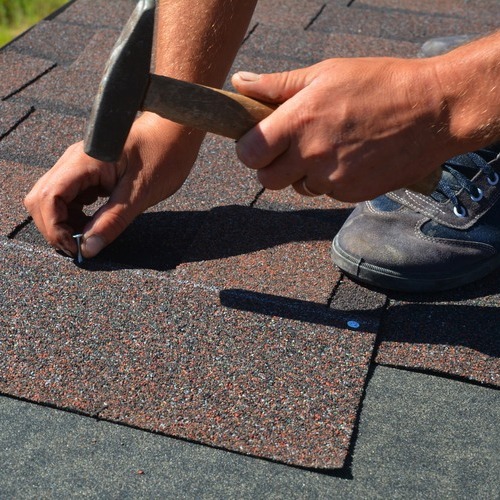 close-up of a worker nailing down asphalt shingle roofing